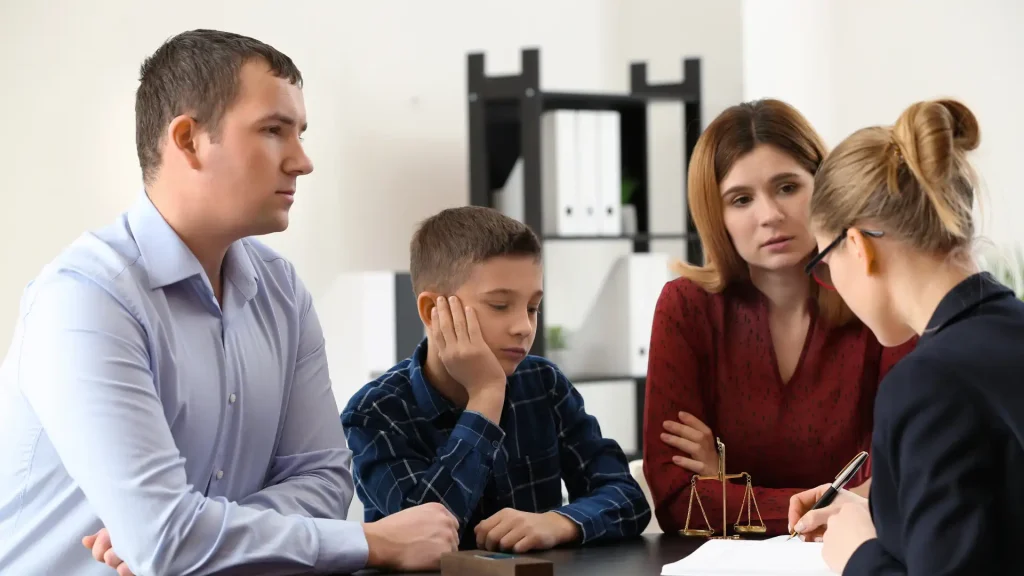 Sad child sitting between two serious-looking parents in a legal setting.
